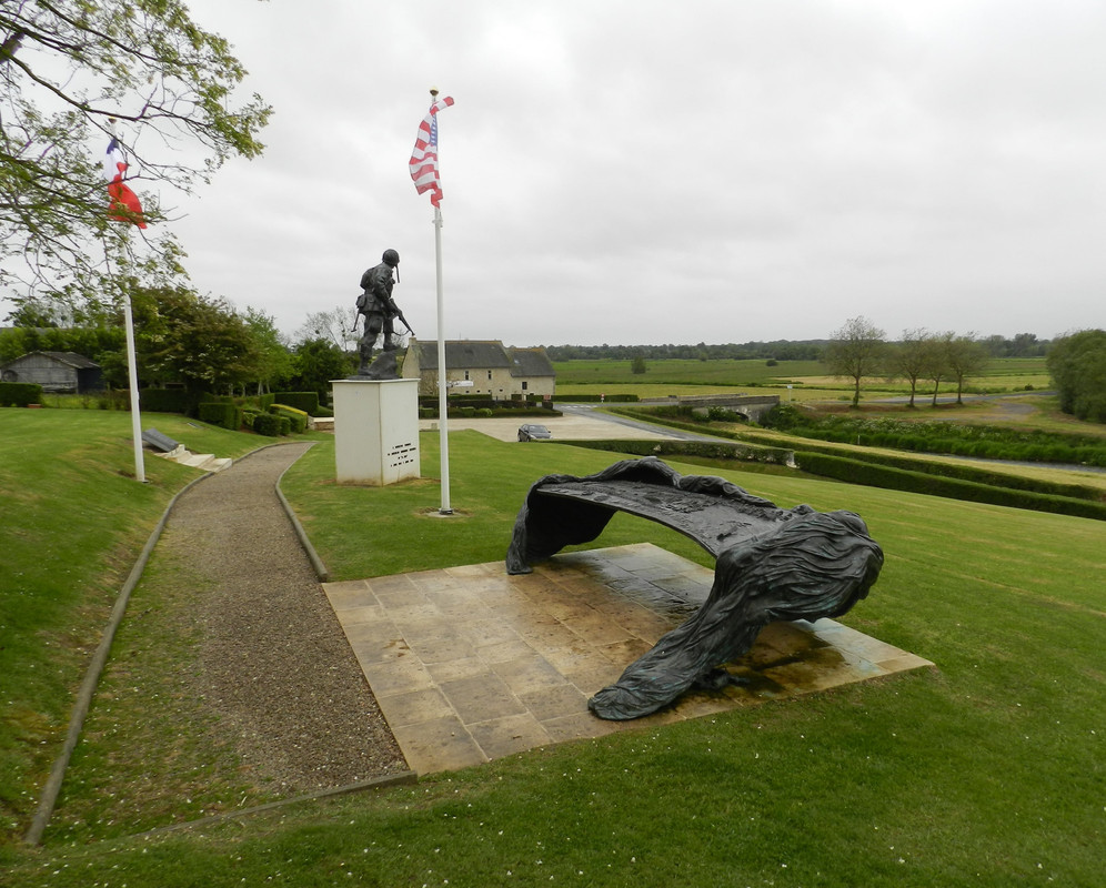 Conjunto memorial compuesto por varias placas conmemorativas, paneles descriptivos y una estatua de un Iron Mike en el puente sobre el río Merderet